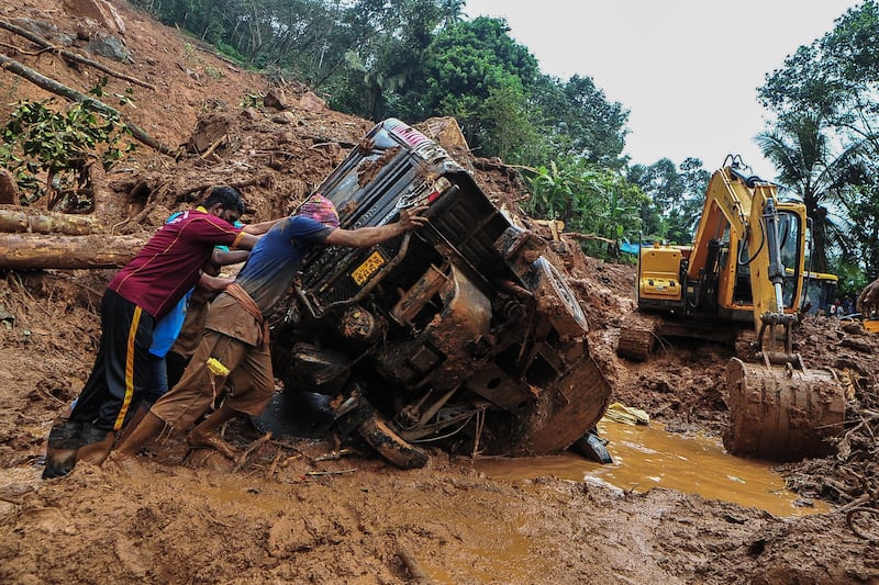 Rescue workers push an overturned vehicle stuck in the debris at the site of a landslide caused by heavy rains in Kokkayar. AFP