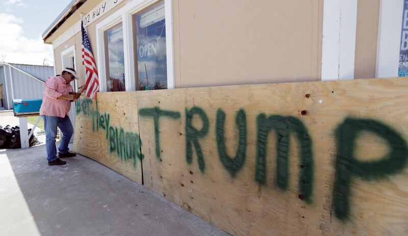 John Murray attaches a US flag to a sign reading "Bet They Blame Trump" at his business damaged in the wake of Harvey in Rockport, Texas. Murray created the sign in hopes president Donald Trump would visit Rockport during his Texas visit, but he did not expect him to make the trip. Eric Gay / AP Photo