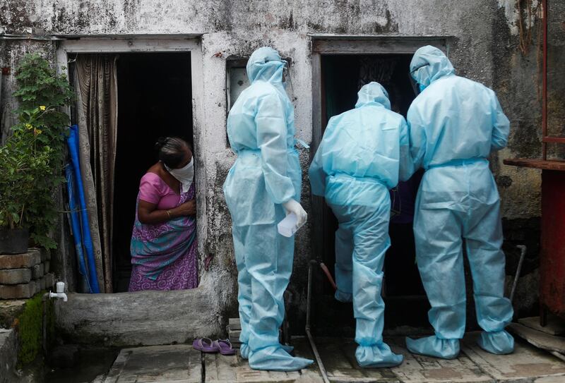 A woman watches as healthcare workers wearing personal protective equipment check the temperature of residents of a slum during a check-up camp. Reuters