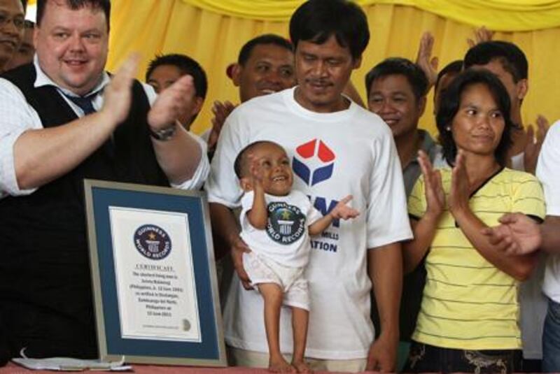 epa02776243 Craig Glenday of Guinness World  Records (L) celebrates with Junrey Balawing, who is celebrating his 18th birthday (C) standing next to a Guinness World  Records ceritificate, crowned as the shortest living man during a ceremony inside a municipal hall in Sindangan, Zamboanga del Norte, southern Philipipines on 12 June 2011. Junrey, a 23.59 inches or 59.93 centimeters tall , who struggles to walk and can't stand too long, replaced Nepalese Khagendra Megar, who stands 26.4 inches for distinction. 'We are very proud of him,' said his mother Concepcion.  EPA/DENNIS M. SABANGAN *** Local Caption ***  02776243.jpg