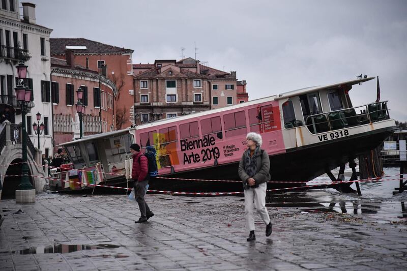 People walk past a stranded taxi boat on Riva degli Schiavoni, after it was washed away during an exceptional overnight "Alta Acqua" high tide water level. AFP