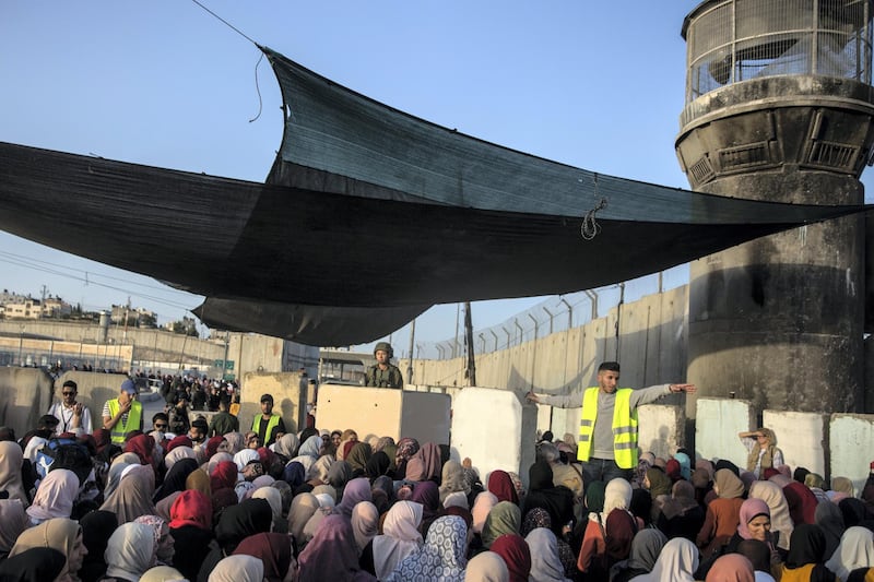 An Israeli female soldier behind a concrete barrier as Palestinian women of all ages  cue in lines to cross  the Qalandia checkpoint to pray in Jerusalem on May 17,2019. The Friday mornings during Ramadan is the most crowded foot traffic time at Qalandia, as tens of thousands of Palestinians from all around the West Bank cross through to pray in Jerusalem. Photo by Heidi Levine for The National).