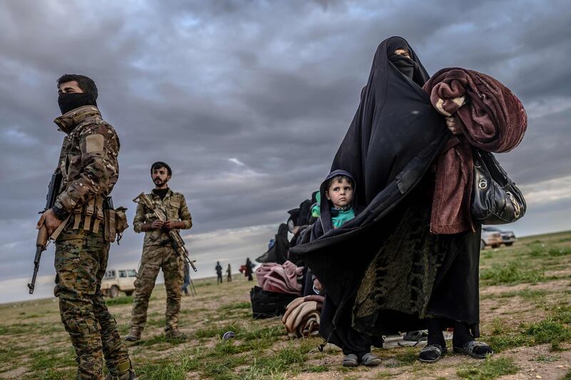 Members of the Syrian Democratic Forces stand guard as a woman walks with a child after they left ISIS's last holdout of Baghouz, in Syria. AFP