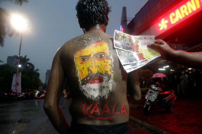 An Indian man with the face of Indian movie superstar Rajinikanth painted on his back poses for a picture outside a cinema hall before heading to watch Rajinikanth's new movie Kaala in Mumbai. Rajanish Kakade / AP Photo