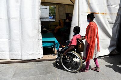 This photograph taken on April 7, 2020 shows wife of 38-year-old patient Upender Safi (C) pushing his wheelchair at a night shelter setup by Delhi government outside the All India Institute of Medical Sciences (AIIMS) during a government-imposed nationwide lockdown as a preventive measure against the COVID-19 coronavirus, in New Delhi. - The capacity of medical facilites around the world has been stretched by the surge of COVID-19 patients as outbreaks worsen in many countries. It can cause people with other life-threatening diseases to miss out on vital care -- especially in places like India, where healthcare systems are shakier. Dozens of people with serious medical conditions are camped outside India's national medical institute in tents set up by the Delhi government. (Photo by Prakash SINGH / AFP) / To go with FOCUS 'HEALTH-VIRUS-INDIA' by AISHWARYA KUMAR.