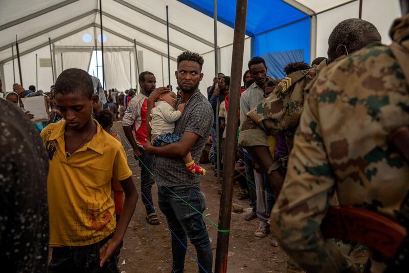 A man who fled the conflict in the Ethiopia's Tigray region holds his baby as he stands in line to register his name at Hamdayet Transition Center, eastern Sudan. AP Photo