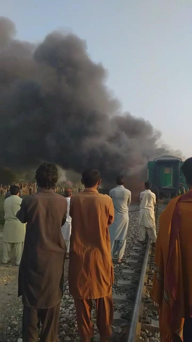 Men look at a burning train after a gas canister passengers were using to cook breakfast exploded, near the town of Rahim Yar Khan in the south of Punjab province, Pakistan, in this still image take from video obtained from social media.  REUTERS