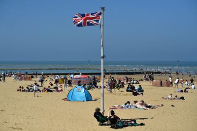 A Union flag flutters in the breeze as sunbathers take advantage of the fine weather on the beach on the coast at Margate, east of London on May 31, 2021, as fine and dry conditions continue in the UK on what could be the hottest day of the year so far.  / AFP / Ben STANSALL
