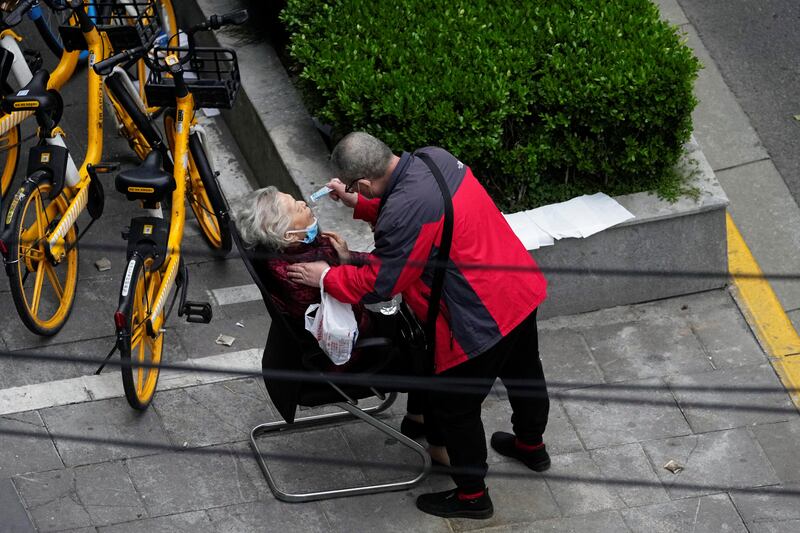 A man helps a woman to consume a packet of traditional Chinese medicine, as she sits by the side of a road outside a residential compound. Reuters