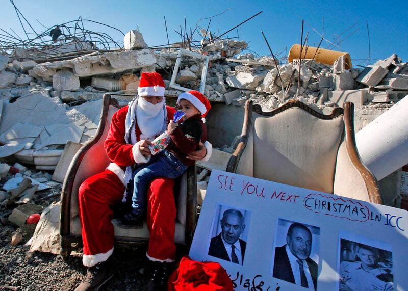 A Palestinian man dressed as father Christmas holds a child  by the rubble of a house demolished by Israel in West Bank. AFP