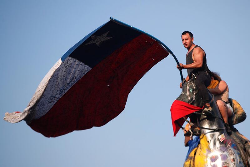 Protesters wave a Chilean flag on top of the statue of General Manuel Jesus Baquedano during a demonstration at the Plaza Italia in Santiago, Chile.  EPA