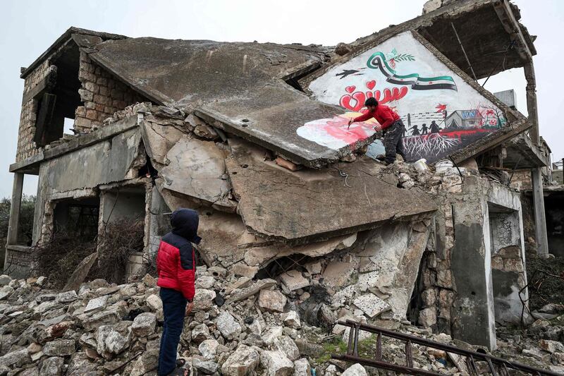 A boy watches as a man paints a mural on the roof of a collapsed building in Binnish to commemorate the ninth anniversary of the Syrian war. AFP