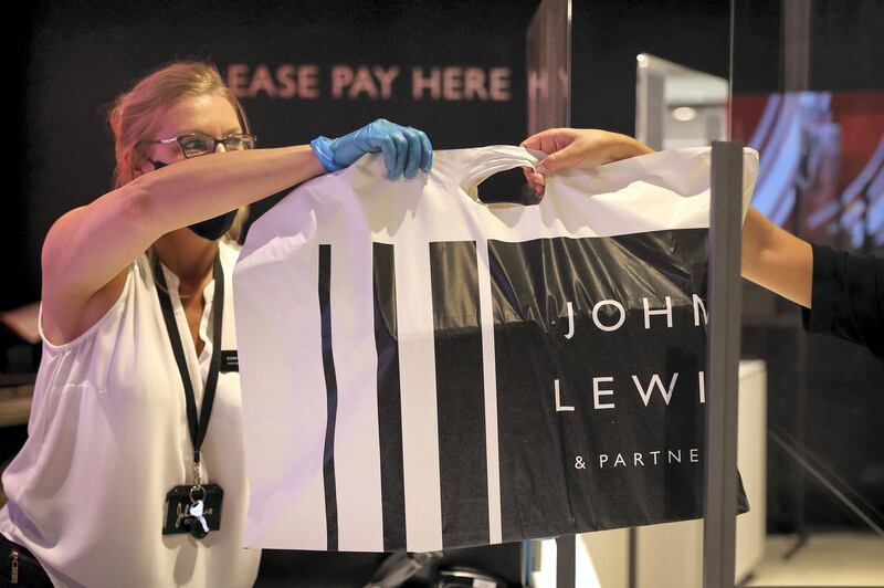 An employee wearing a protective face mask and gloves hands a customer a branded shopping bag through a perspex screen inside a John Lewis Partnership Plc department store in London, U.K., on Thursday, July 23, 2020. U.K. Prime Minister Boris Johnson had resisted making masks mandatory until July 13, when his government announced that face coverings will be compulsory in stores as of July 24. Photographer: Simon Dawson/Bloomberg via Getty Images