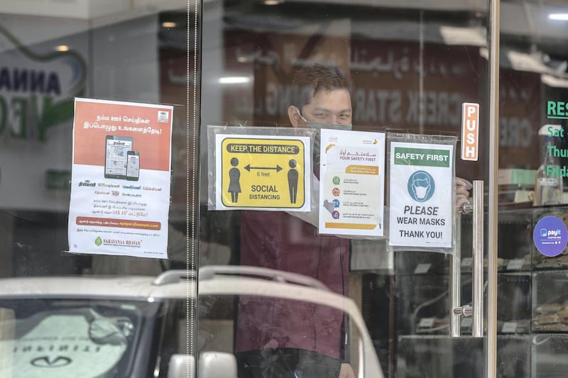 DUBAI, UNITED ARAB EMIRATES. 15 JUNE 2020. STANDALONE. Bur Dubai life during COVID-19.  A door man smile at the camera while waiting oinside a restaurant for patrons to arrive with COVID-19 warning outside. (Photo: Antonie Robertson/The National) Journalist: None. Section: National.