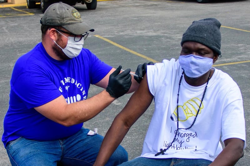 In this April 7, 2021, photo provided by Neighborhood Health, Dr. Pete Cathcart vaccinates Deng Autiak in Nashville. With vaccine supplies increasing in the U.S., the shots are finally reaching thousands of Americans who are homeless. In Nashville, many organizations have set a goal of bringing vaccine to everyone experiencing homelessness by Memorial Day. (Jeremy McCraw/Neighborhood Health via AP)