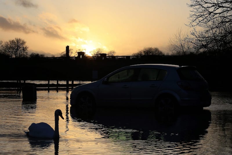 A swan passes a car abandoned in flood water in a car park after the River Trent burst its banks, in Gunthorpe, Nottinghamshire, in central England.  AFP