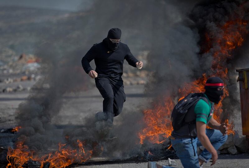 A masked Palestinian demonstrator jumps over burning tires during clashes with Israeli border police near Ramallah, West Bank. AP Photo