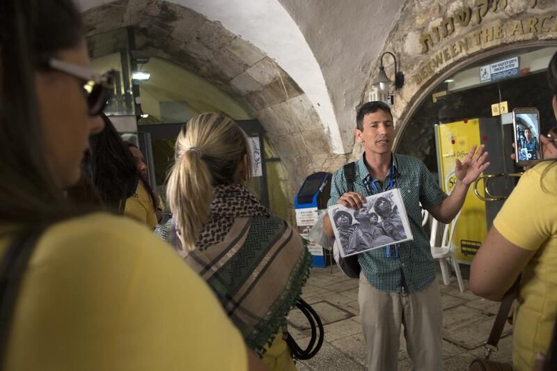An Israeli tour guide shows one of the most iconic photographs of the 1967 Arab-Israeli war to his group of tourists from the Philippines near the entrance to the Western Wall in the Old City of Jerusalem on May 20, 2017. The black and white photograph of three Israeli paratroopers standing at the Western Wall was taken on June 7,1967 by Time Life Israeli photographer David Rubinger. Heidi Levine for The National