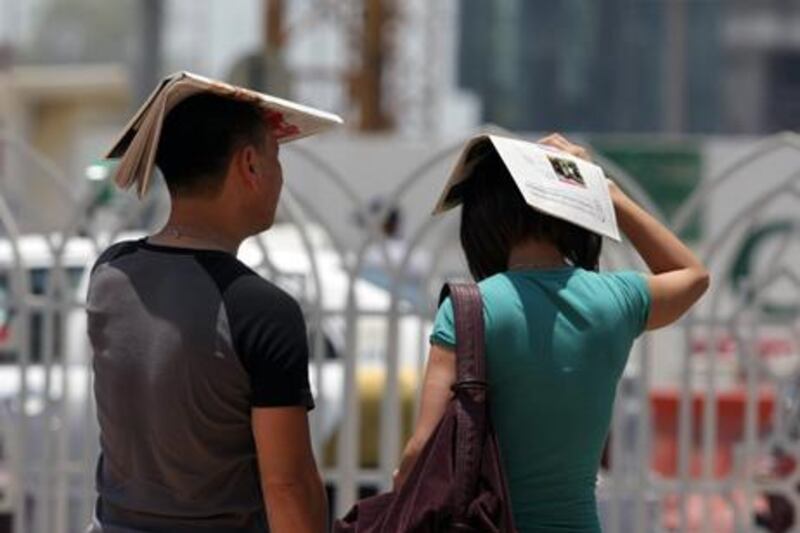 United Arab Emmirates - Abu Dhabi - A man and a woman use a paper to  protect from the sun and the hot temperatures in Sheikh Hamdan Bin Mohammad St ( Jaime Puebla / The National ) *** Local Caption ***  JP 04 HotÊTemperatures.jpg