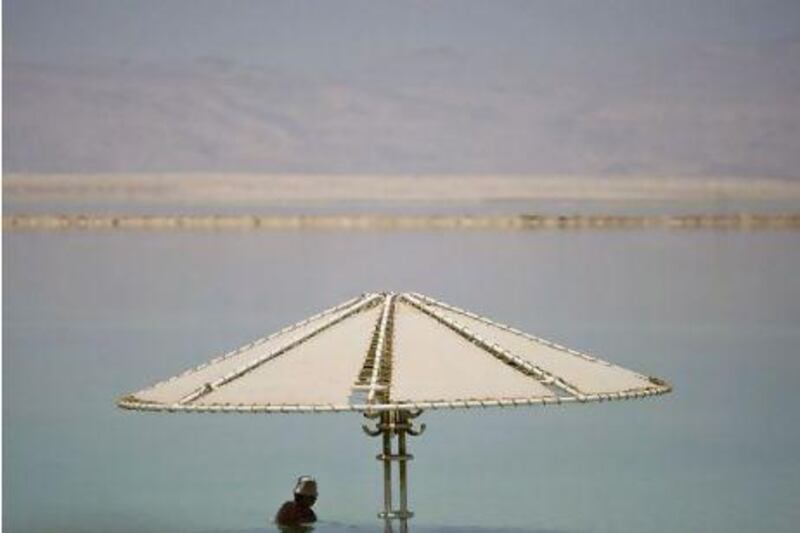 A bather wades in the waters of the Dead Sea near Neve Zohar, Israel. Israel's tourism and environmental protection ministers are endorsing a $2bn plan to chip off the salt buildup on the part of the lake that is rising and send it by conveyor belt to the northern end, which is dropping. Ariel Schalit / AP Photo