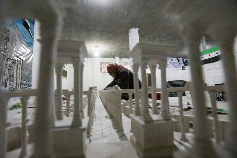 A man assists Ali Saleh (unseen), a 58-year-old displaced Syrian originally from Palmyra, as they build from memory a wood and gypsum model of a prominent archaeological landmark of his home city that was heavily damaged by Islamic State (IS) militants, at a workshop home in the rebel-held city of al-Bab northwest of Aleppo in northern Syria on January 14, 2021. - Ten years of Syria's civil war have robbed Saleh of his home in the desert city, his three sons and daughter, and the last of his poor hearing, his family says. But he still vividly remembers Palmyra's ruins, where he accompanied restoration and excavation teams for 25 years, before the Islamic State group overran the city in 2015. (Photo by Bakr ALKASEM / AFP)