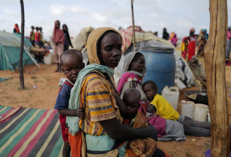 A Sudanese woman who fled the conflict sits with her children on the ground beside makeshift shelters in Adre, Chad.