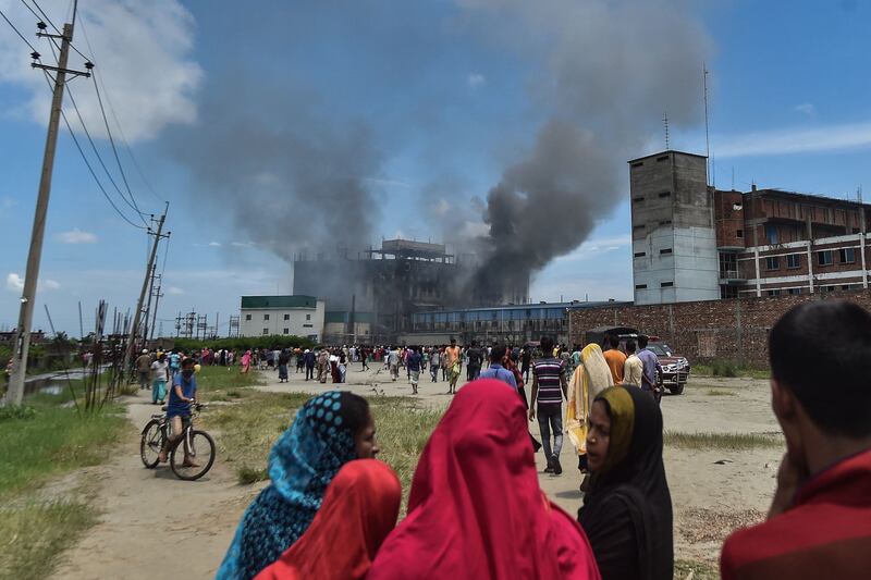 Onlookers watch as smoke bellows from a massive fire that broke out a day before in a beverage and food factory in Rupganj in the district Narayanganj that has reportedly claimed 43 lives so far.