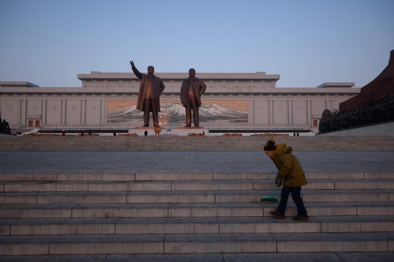 A boy sweeps steps before the statues of Kim Il Sung and Kim Jong Il. AFP