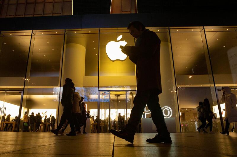 FILE - In this Dec. 13, 2019, file photo a man looks at his phone as he walks past a store of US tech giant Apple in a retail district in Beijing. Apple reports financial earns on Tuesday, Jan. 28, 2020.(AP Photo/Ng Han Guan, File)