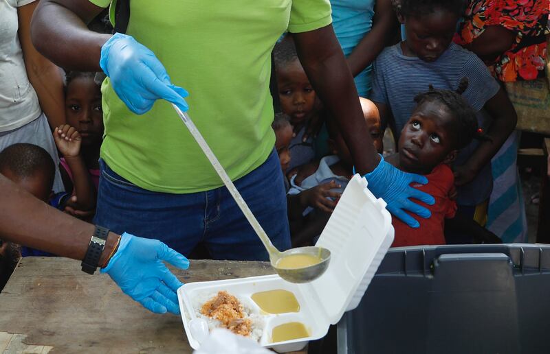 A server ladles soup into a container as children queue for food at a shelter for families displaced by gang violence, in Port-au-Prince, Haiti. AP