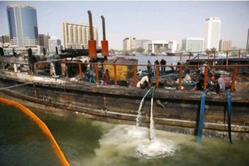 Recovery crew pump water from the burnt hull of the dhow.