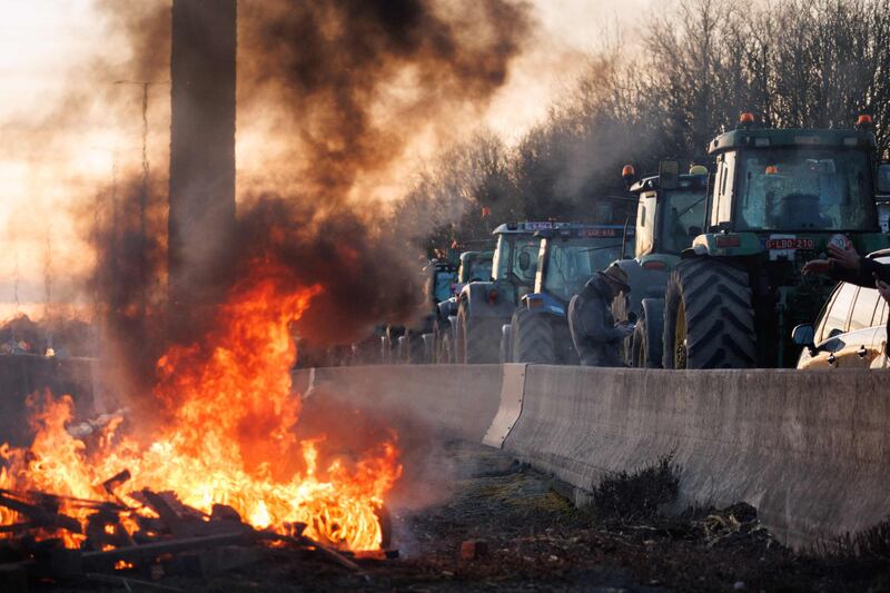 A convoy of tractors passes by a fire lit by farmers, during a protest at the Daussoulx interchange, in Belgium. AFP