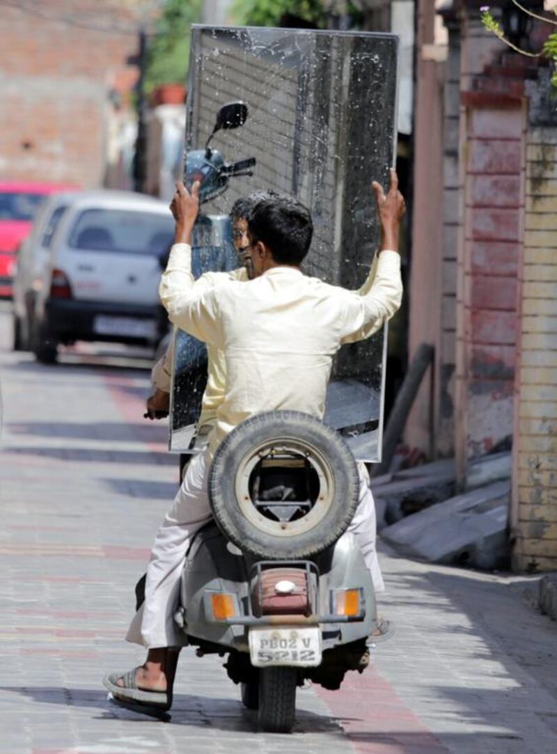 A man sits holding a mirror on the rear seat of a scooter in a street in Amritsar.  Raminder Pal Singh / EPA