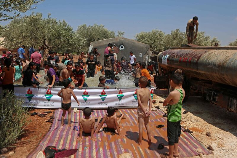 Syrian children play in a portable swimming pool set up by volunteers, at a camp for the displaced in the rebel-held town of Kafr Yahmul in Idlib. 