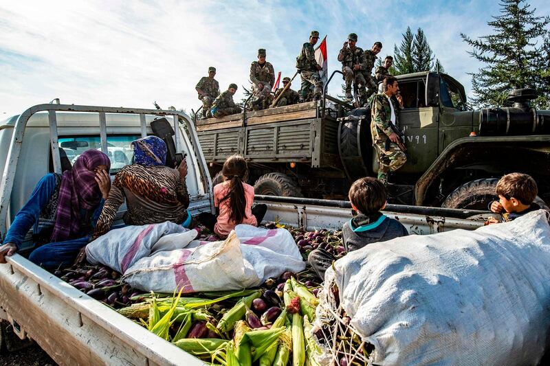 Syrian government soldiers ride in the back of a truck with national flags past a pickup truck carrying women and children seated above harvested aubergines and maize, as government forces deploy for the first time in the eastern countryside of the city of Qamishli in the northeastern Hasakah province. AFP