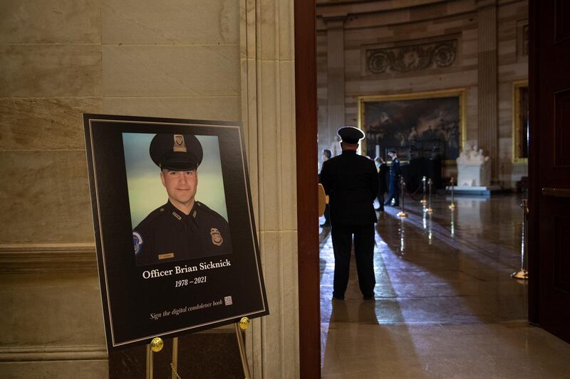 FILE - In this Feb. 2, 2021, file photo a placard is displayed with an image of the late U.S. Capitol Police officer Brian Sicknick on it as people wait for an urn with his cremated remains to be carried into the U.S. Capitol to lie in honor in the Capitol Rotunda in Washington. Federal investigators probing the death Sicknick, a U.S. Capitol Police officer killed in the Jan. 6 riot, have zeroed in on a suspect seen on video appearing to spray a chemical substance on the officer before he later collapsed and died, two people familiar with the matter told The Associated Press. (Brendan Smialowski/Pool via AP, File)