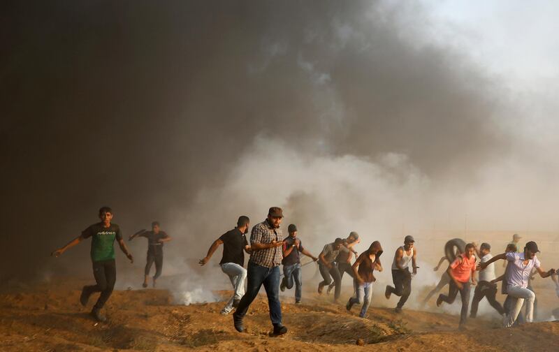 Protesters run to cover from tear gas fired by Israeli troops, while others burn tires near fence of the Gaza Strip border with Israel, during a protest east of Gaza City. AP Photo