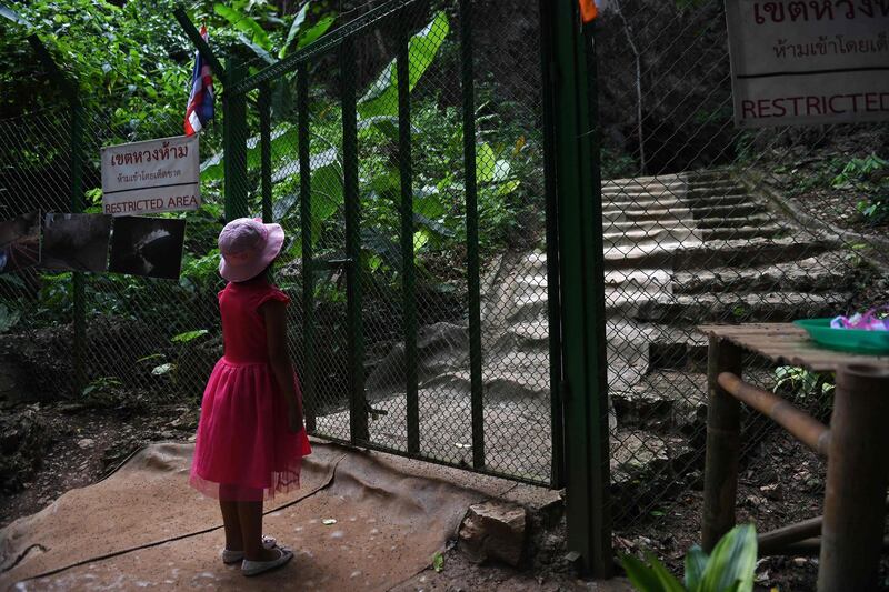 This picture taken shows a girl looking through a gate at the entrance of the Tham Luang cave.  AFP