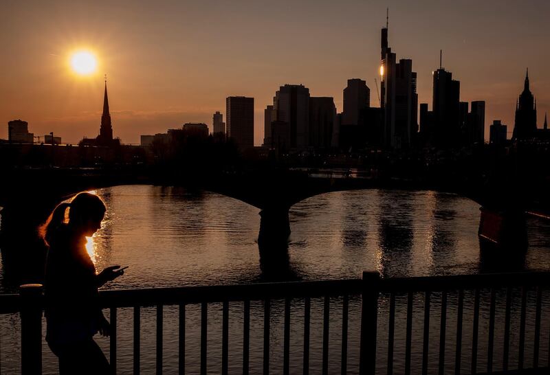 The buildings of the banking districts are seen as a woman walks by at the River Rhine in Frankfurt, Germany. AP Photo