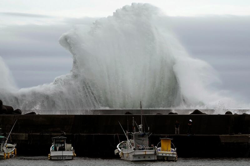 Men look at fishing boats as surging waves hit against the breakwater in town of Kiho, Mie Prefecture. AP