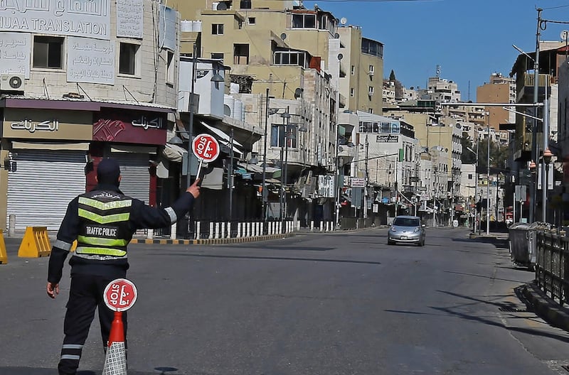 A police officer holds up a stop sign as a car approaches in an almost-deserted street in Jordan's capital Amman, during a coronavirus lockdown. AFP