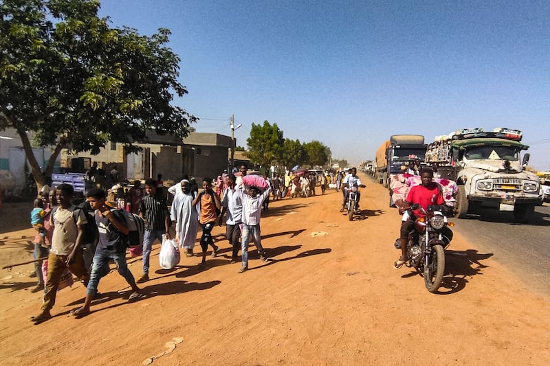 People displaced by the conflict in Sudan walk with their belongings along a road in Wad Madeni, the capital of Al Gezira state, on December 16, 2023.  AFP