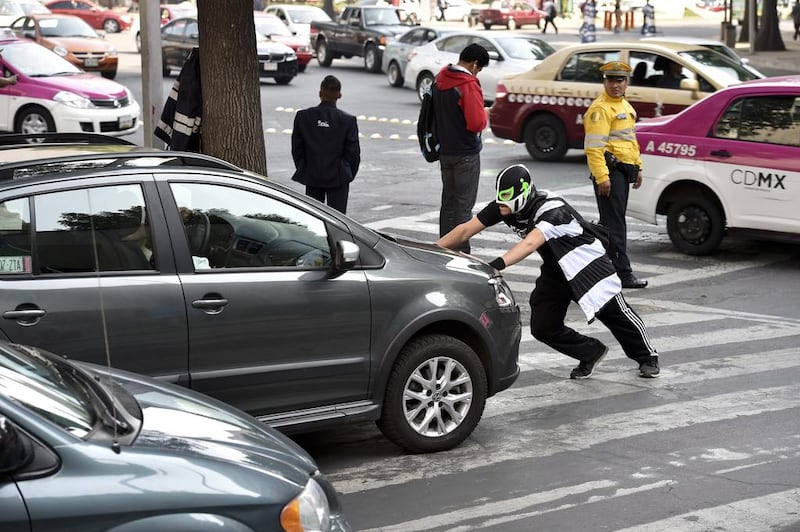 A man who calls himself 'Peatonito' and dresses as a wrestler, pushes a car as he performs his routine in the streets of Mexico City on April 21, 2015. Peatonito is a character who resembles a superhero trying to raise drivers' awareness so thay they respect crosswalks on the streets of Mexico City.  Yuri Cortez/AFP Photo