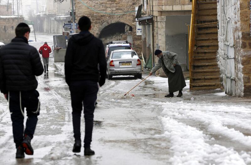 A Palestinian man clears a street from slushy snow in the West Bank city of Hebron. EPA