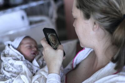 a New mom takes a picture of her newborn baby boy on her phone.
