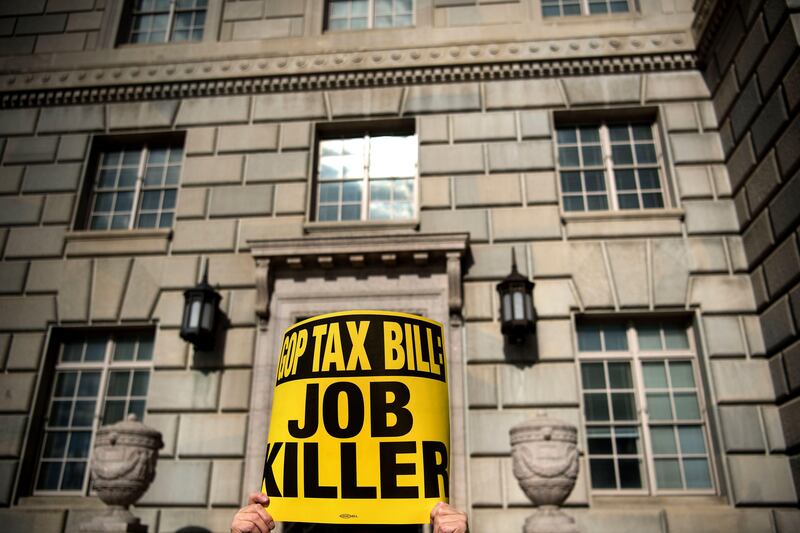A protester holds a sign as he gathers with others to protest the Republican tax reform plan outside the Department of Commerce on November 10, 2017 in Washington, DC. / AFP PHOTO / Brendan Smialowski