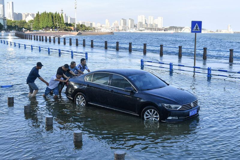 People push a car on a flooded street as waves caused by Typhoon In-Fa surge over a barrier along the coast in Qingdao in China's eastern Shandong province.