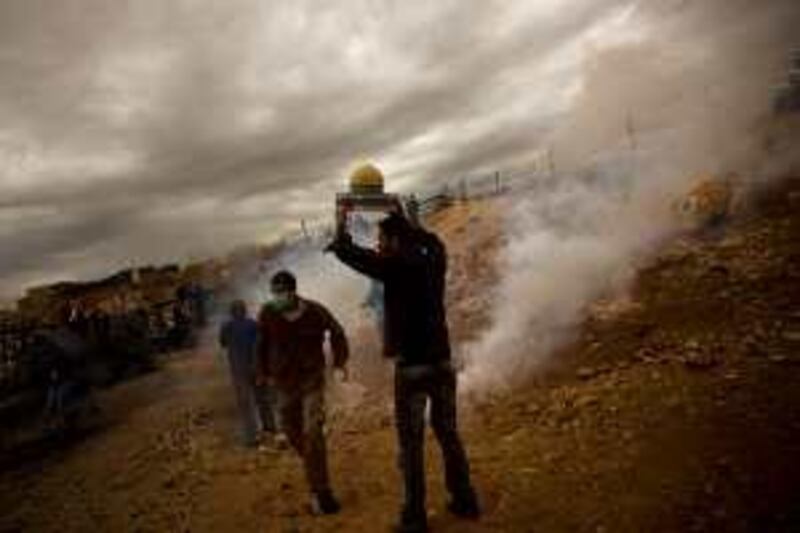 A Palestinian protestor holds up a model of the Dome of the Rock as Israeli border police fire tear gas during a demonstration against the separation barrier on Friday, October 30, 2009, in Bilin, West Bank. (Warrick Page/The National) *** Local Caption ***  20091030WP_bilin_demo_001.jpg