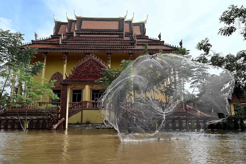 A man casts a fishing net into floodwaters at a temple on the outskirts of Phnom Penh, Cambodia, on October 21, 2023. AFP