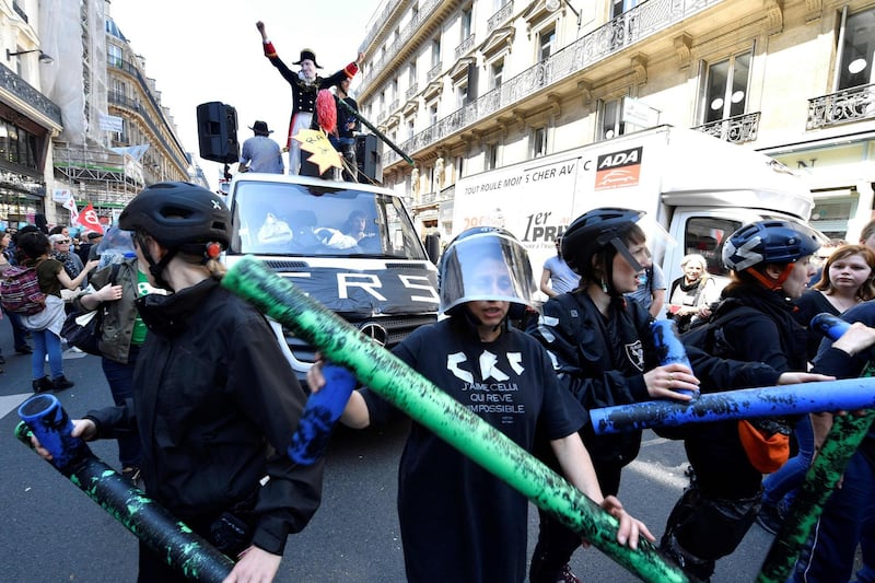 Protesters wearing helmets and holding fake baton march during "The party for Macron" (La Fete a Macron) rally called to protest against policies of the French president on the first anniversary of his election, on May 5, 2018 in central Paris.  / AFP PHOTO / GERARD JULIEN